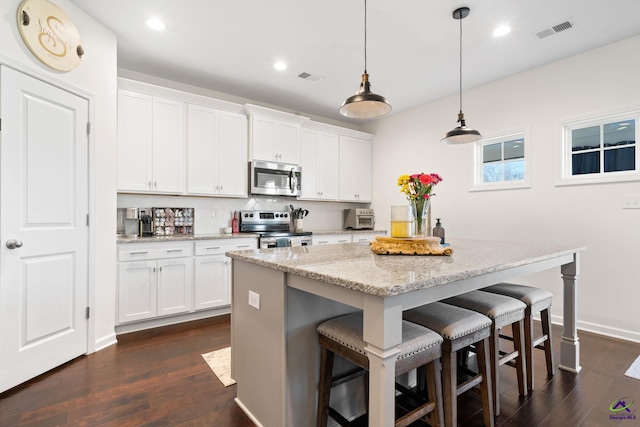 kitchen with light stone counters, an island with sink, pendant lighting, stainless steel appliances, and white cabinets