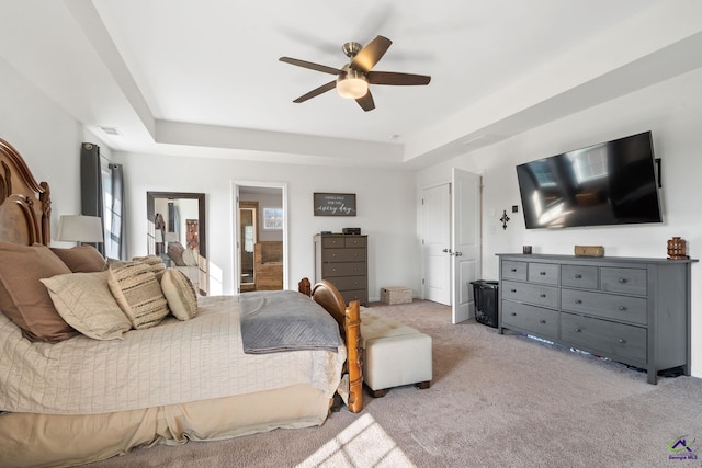 carpeted bedroom featuring ceiling fan, ensuite bathroom, and a tray ceiling