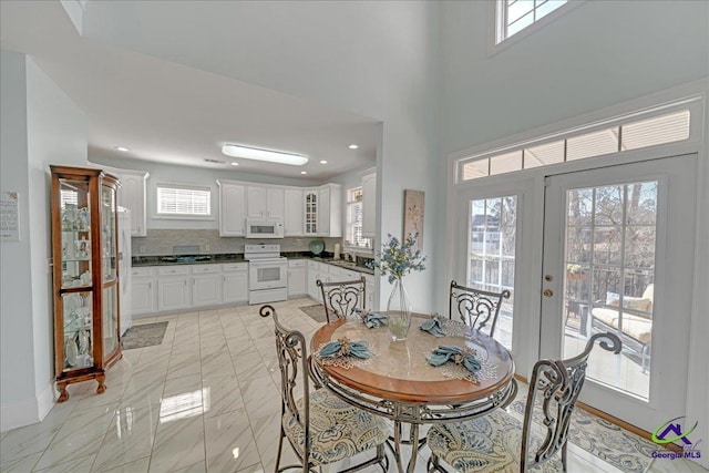 dining space featuring sink, a towering ceiling, french doors, and a healthy amount of sunlight