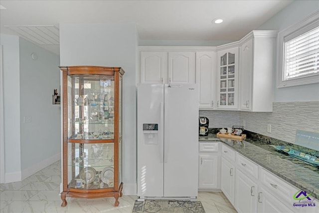 kitchen with tasteful backsplash, white fridge with ice dispenser, dark stone countertops, and white cabinets