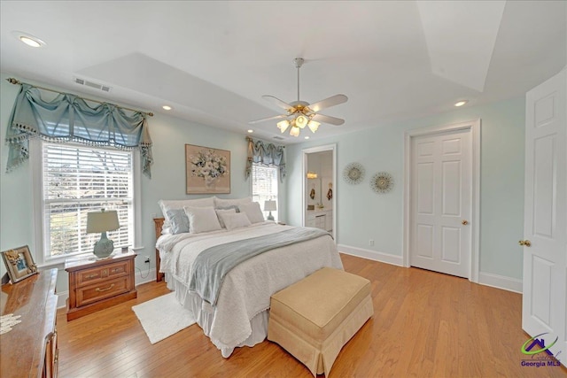 bedroom featuring ceiling fan, a tray ceiling, light wood-type flooring, and ensuite bath