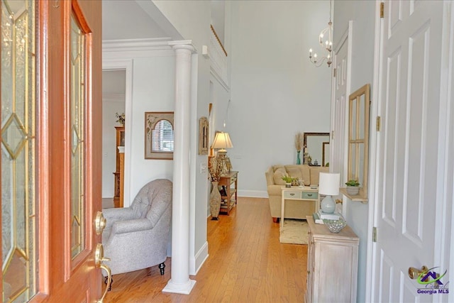 entryway with ornate columns, a chandelier, a high ceiling, ornamental molding, and light wood-type flooring