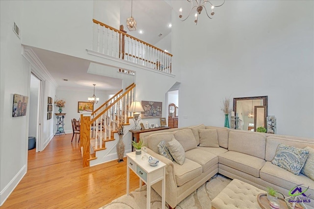 living room with wood-type flooring, a towering ceiling, a notable chandelier, and ornamental molding