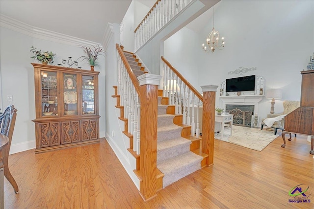 staircase with crown molding, a towering ceiling, an inviting chandelier, and hardwood / wood-style floors