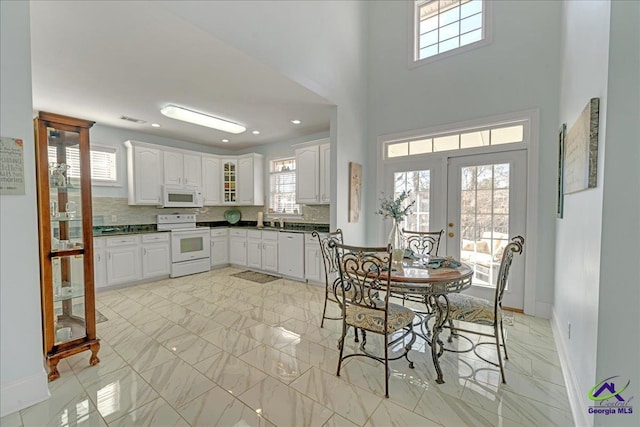 kitchen featuring french doors, tasteful backsplash, white cabinets, white appliances, and a high ceiling