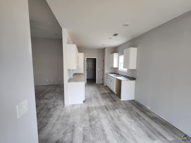 kitchen with sink, white cabinets, light stone counters, and light hardwood / wood-style flooring