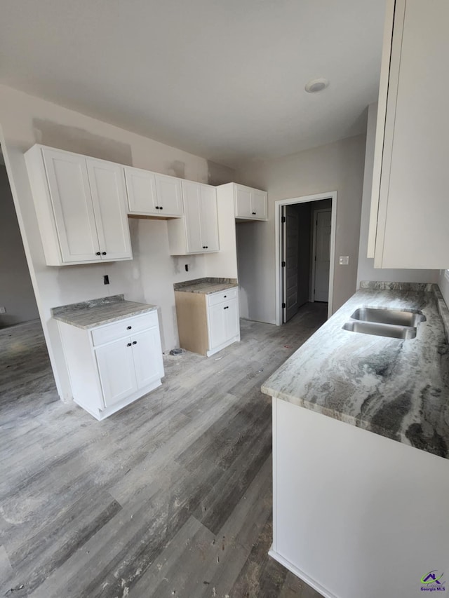 kitchen featuring sink, wood-type flooring, light stone countertops, and white cabinets