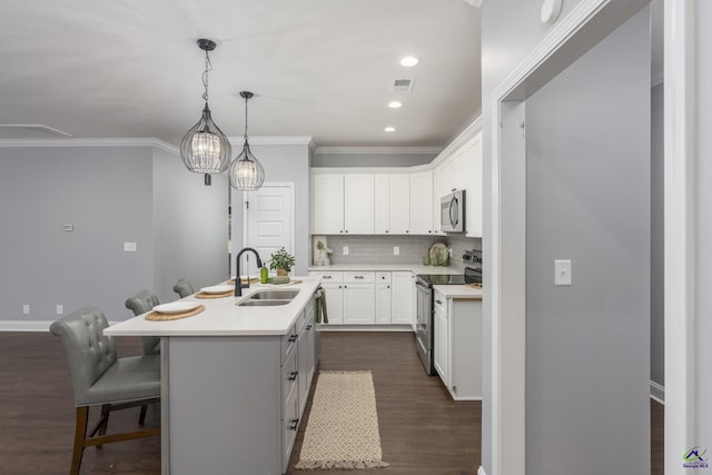 kitchen with appliances with stainless steel finishes, an island with sink, sink, white cabinets, and a kitchen breakfast bar