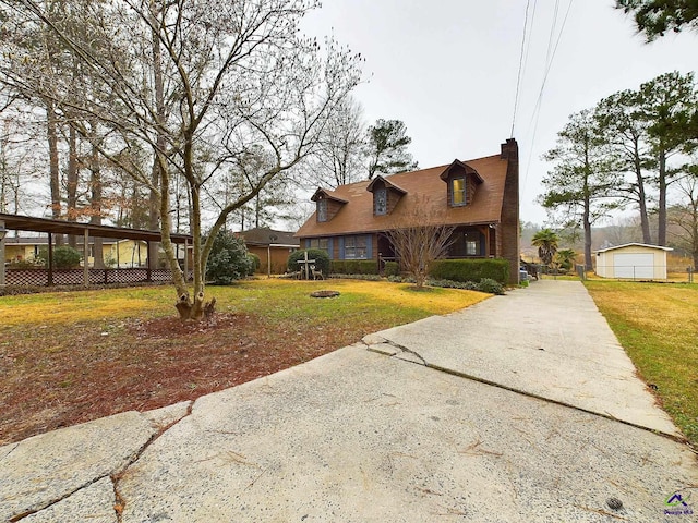 new england style home featuring a chimney, concrete driveway, and a front lawn