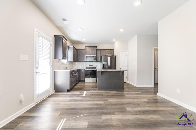 kitchen featuring appliances with stainless steel finishes, sink, a center island, hardwood / wood-style flooring, and tasteful backsplash