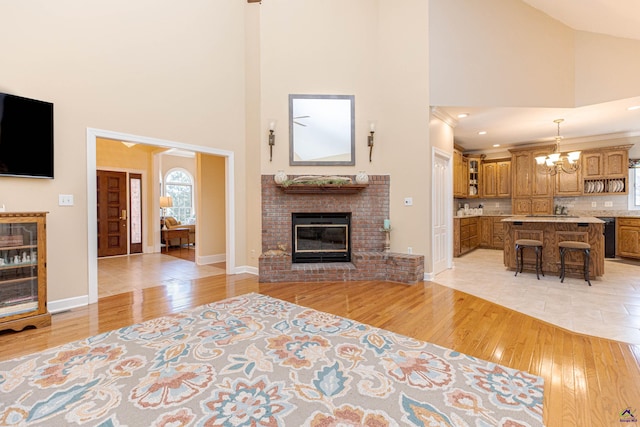 unfurnished living room featuring a brick fireplace, high vaulted ceiling, a notable chandelier, and light wood-type flooring