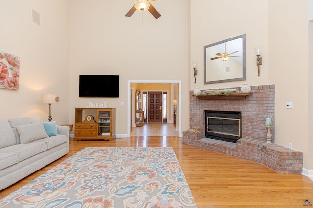 living room with a brick fireplace, hardwood / wood-style flooring, ceiling fan, and a towering ceiling