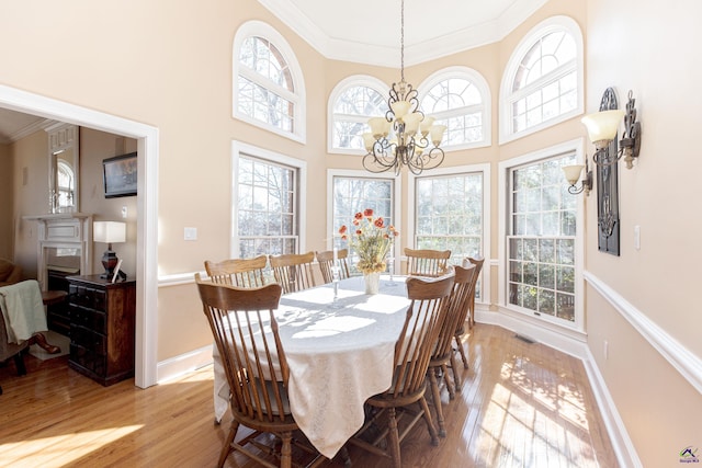 dining room featuring a notable chandelier, a towering ceiling, light hardwood / wood-style flooring, and ornamental molding