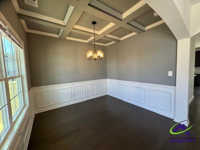 empty room featuring beamed ceiling, coffered ceiling, dark hardwood / wood-style floors, and an inviting chandelier