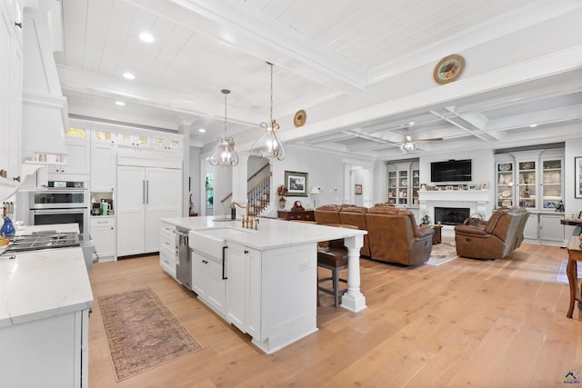 kitchen featuring a kitchen island with sink, white cabinets, light stone counters, and decorative light fixtures