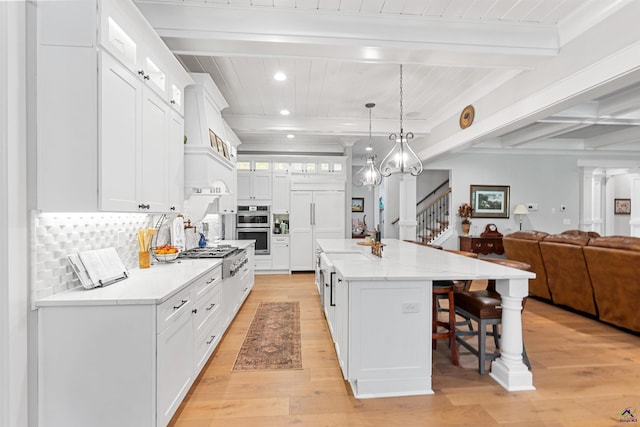 kitchen featuring white cabinetry, hanging light fixtures, a center island with sink, beamed ceiling, and stainless steel appliances