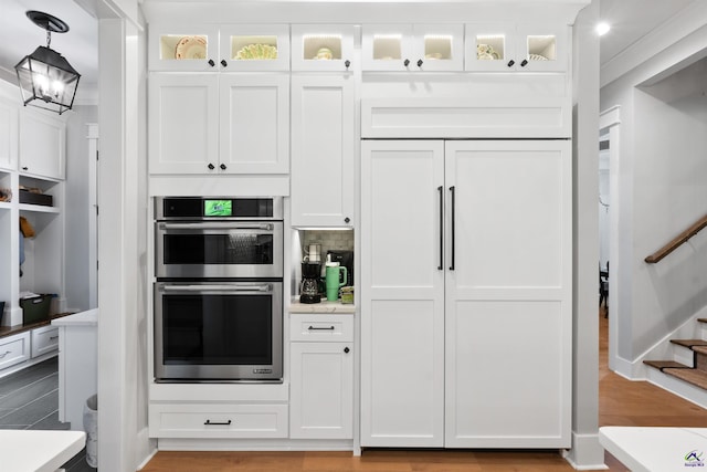 kitchen with pendant lighting, white cabinets, light hardwood / wood-style flooring, and stainless steel double oven