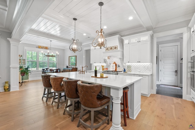 kitchen featuring white cabinetry, tasteful backsplash, decorative light fixtures, light hardwood / wood-style flooring, and a kitchen island with sink