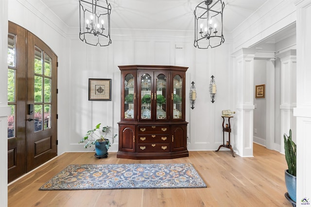 entryway featuring crown molding, light wood-type flooring, an inviting chandelier, and french doors