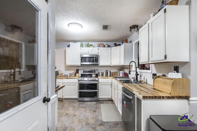 kitchen with butcher block countertops, sink, appliances with stainless steel finishes, a textured ceiling, and white cabinets