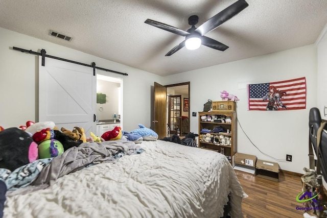 bedroom with dark hardwood / wood-style flooring, ceiling fan, a barn door, and a textured ceiling