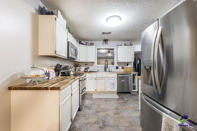 kitchen with butcher block countertops, sink, white cabinetry, stainless steel appliances, and a textured ceiling