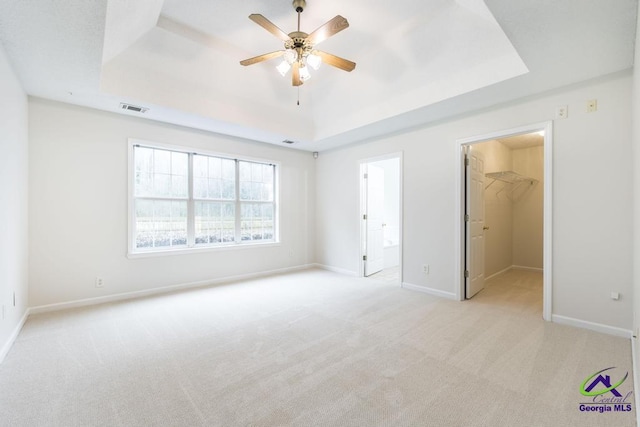 unfurnished bedroom featuring ensuite bath, a raised ceiling, light carpet, a walk in closet, and a closet