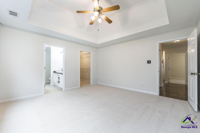 unfurnished bedroom with a walk in closet, light carpet, and a tray ceiling