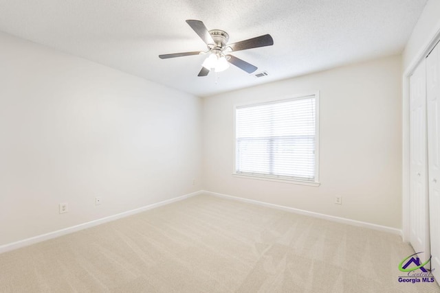 empty room with ceiling fan, light colored carpet, and a textured ceiling