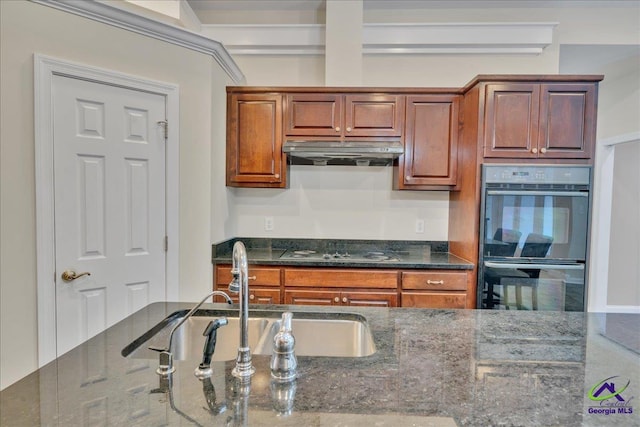 kitchen with stovetop, sink, black double oven, and dark stone counters