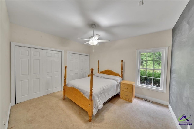 bedroom with multiple closets, light colored carpet, and ceiling fan