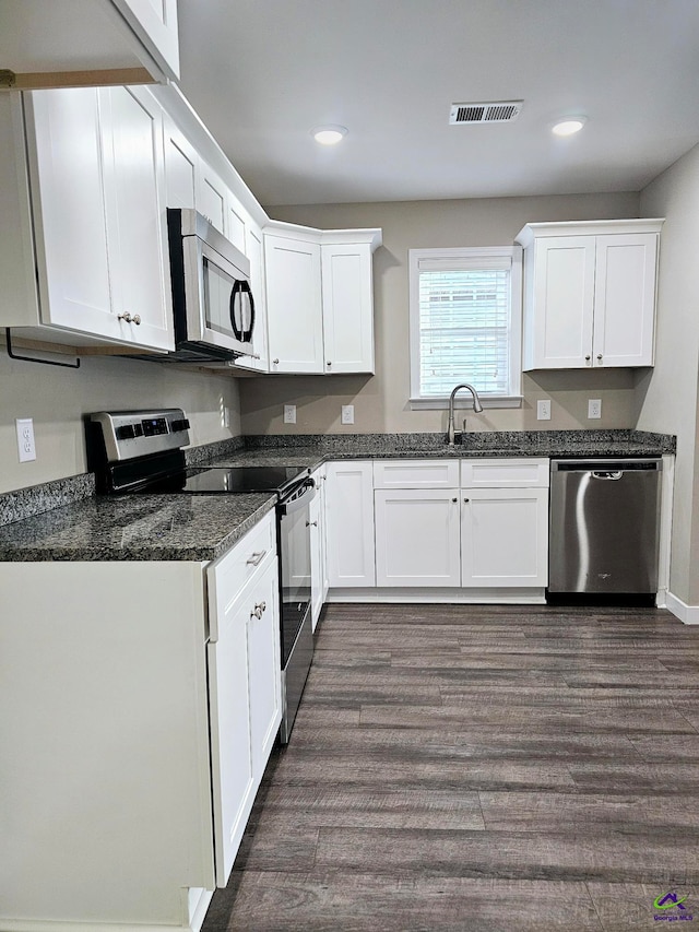 kitchen featuring sink, appliances with stainless steel finishes, dark hardwood / wood-style floors, dark stone counters, and white cabinets