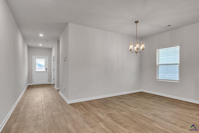 empty room featuring a notable chandelier and light hardwood / wood-style floors