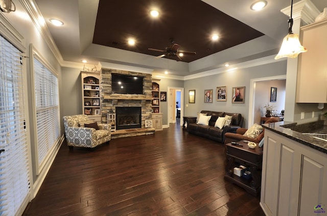 living room featuring dark wood-type flooring, ornamental molding, a raised ceiling, ceiling fan, and a fireplace