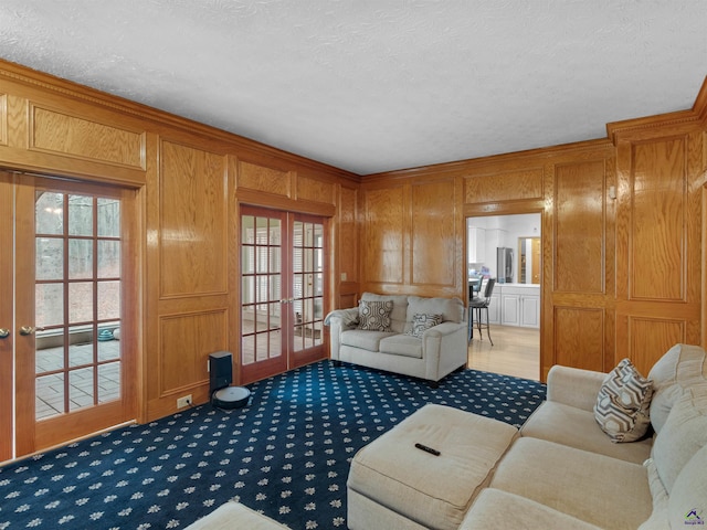 living room with french doors, wood walls, a textured ceiling, ornamental molding, and dark carpet