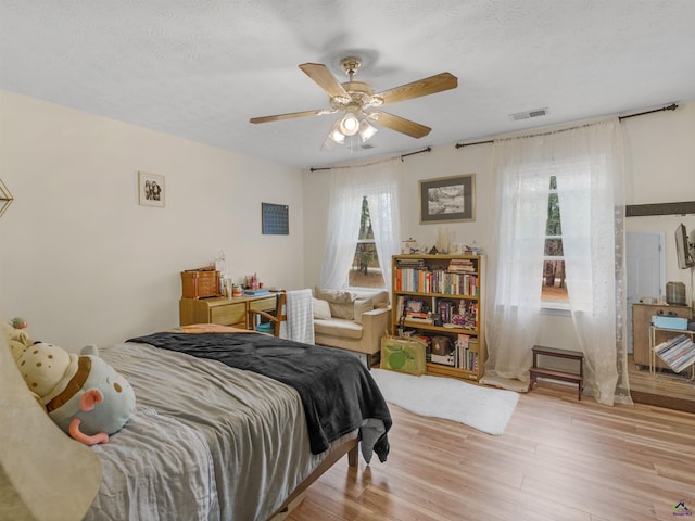 bedroom with ceiling fan, light hardwood / wood-style flooring, and a textured ceiling