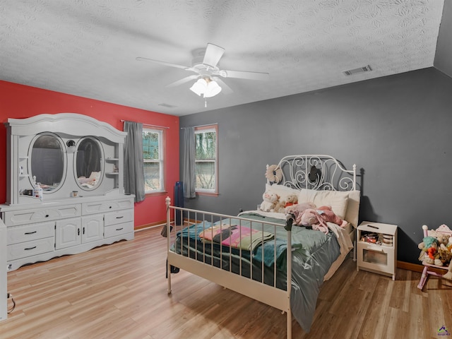 bedroom with ceiling fan, light hardwood / wood-style flooring, and a textured ceiling