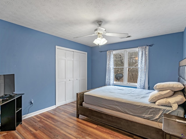 bedroom with dark wood-type flooring, ceiling fan, a closet, and a textured ceiling