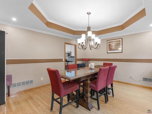 dining space with crown molding, light hardwood / wood-style flooring, a raised ceiling, and a chandelier