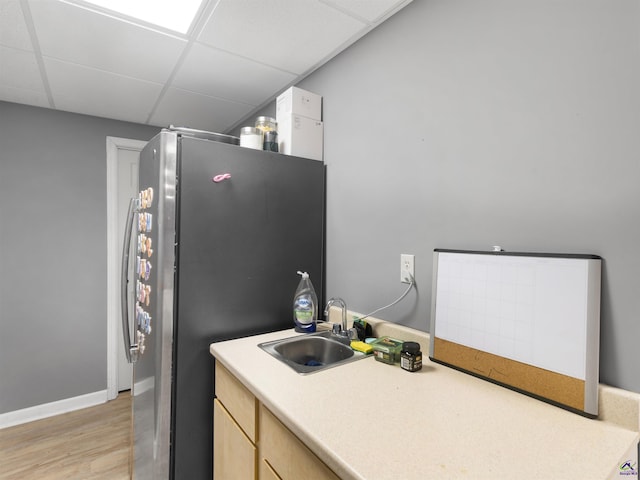 kitchen with a paneled ceiling, light brown cabinetry, stainless steel refrigerator, sink, and light wood-type flooring