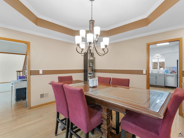 dining room featuring crown molding, a notable chandelier, a raised ceiling, and light wood-type flooring