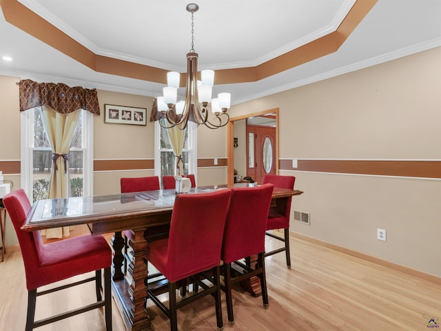 dining area featuring a raised ceiling, ornamental molding, an inviting chandelier, and light wood-type flooring