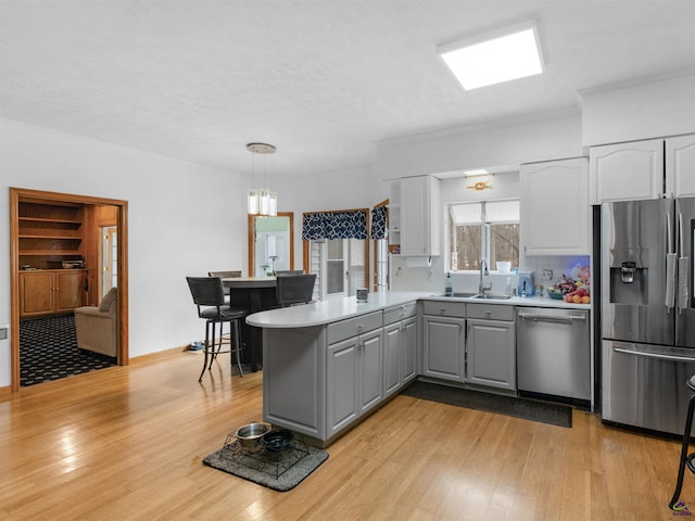 kitchen featuring pendant lighting, sink, gray cabinetry, kitchen peninsula, and stainless steel appliances