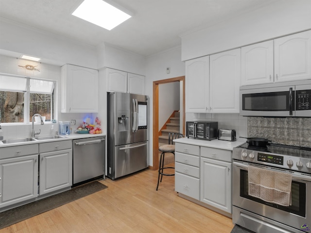 kitchen with sink, white cabinets, backsplash, light hardwood / wood-style floors, and stainless steel appliances