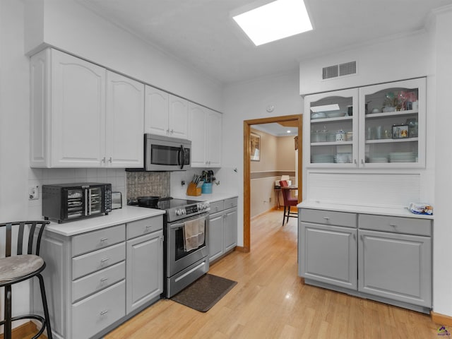 kitchen featuring a breakfast bar, appliances with stainless steel finishes, gray cabinetry, decorative backsplash, and light wood-type flooring