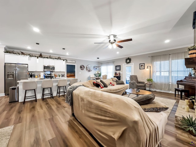 living room with ceiling fan, ornamental molding, and light hardwood / wood-style flooring