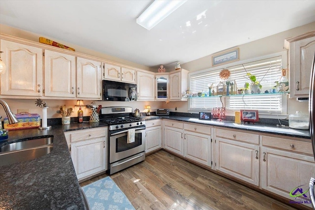 kitchen featuring hardwood / wood-style flooring, stainless steel range with gas cooktop, sink, and dark stone countertops