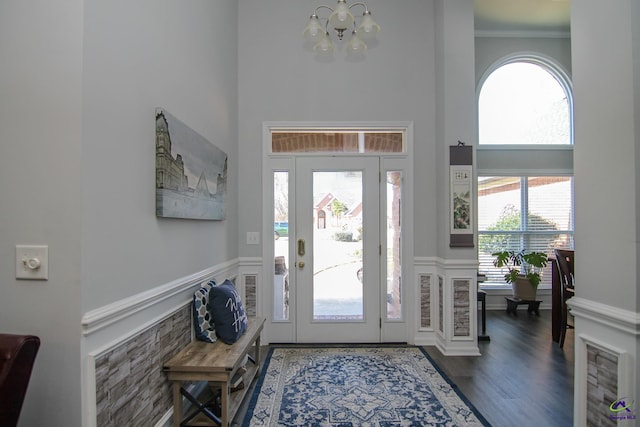 foyer featuring a wainscoted wall, a high ceiling, ornamental molding, wood finished floors, and a chandelier