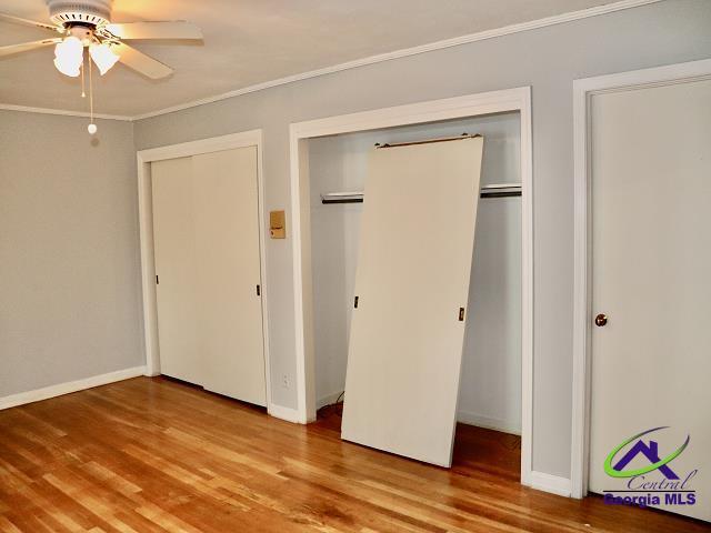 unfurnished bedroom with light wood-style flooring, a ceiling fan, baseboards, multiple closets, and crown molding