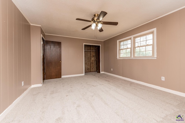 unfurnished bedroom featuring a textured ceiling, baseboards, light colored carpet, and crown molding